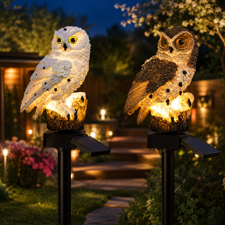 Zwei solarbetriebene Eulenleuchten mit warmweißem LED-Licht im beleuchteten Garten bei Nacht.
